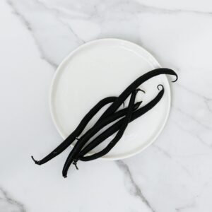 Top view of aromatic vanilla beans on a white plate placed on a marble surface, showcasing minimalist still life photography.